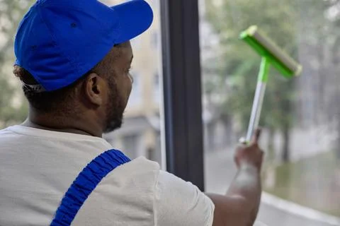 Window cleaner with scraper with sponge for cleaning glass in blue baseball cap Stock Photos