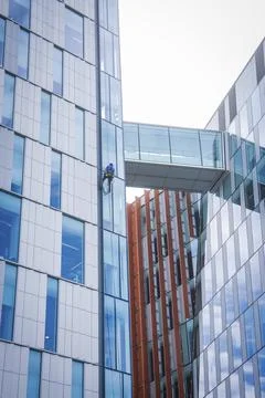Window cleaner working on the glass facade of a high-rise building with a bridge Stock Photos