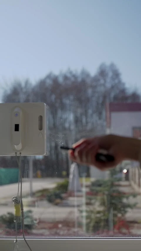 Window cleaning robot is moving while hand with remote control appears in frame Stock Footage 332076637
