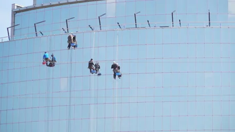 Window cleaning specialists are cleaning the glass outside a skyscraper. Washing Stock Footage 153373446