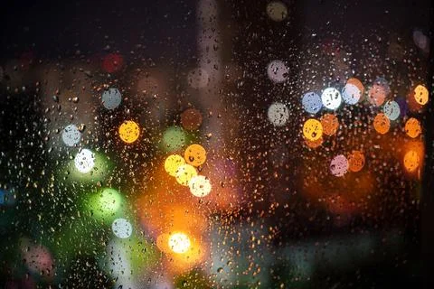 Window covered in raindrops and blurred view colorful bokeh night city lights Stock Photos