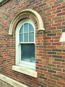A window with a curved top is set into a red brick wall. The glass is slightl 스톡 사진