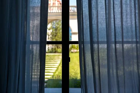 Window frame with blue curtains inside view of backyard with green grass. Stock Photos