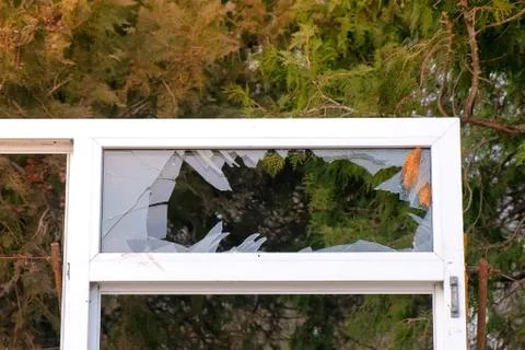 Window frame with broken glass on the background of trees in the city Park. Fotos Stock