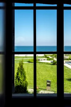 Window frame from the inside of the room with a lawn and a view of the sea. Stock Photos