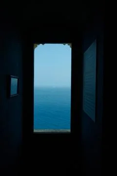 Window frame overlooking blue ocean view and distant horizon from dark interi Stock Photos
