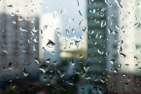 Window glass with rain drops on the background of a blurred cityscape Stock Photos