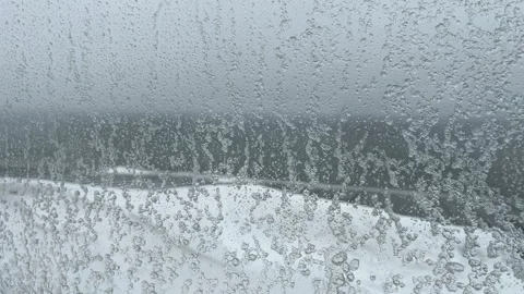 Window glass vibrates as a winter storm blows snow over a roof and sea Stock Footage 327675420