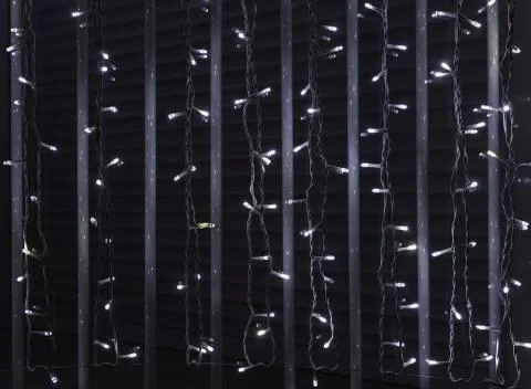 A window with gray bars and dark blinds and with garlands of burning white LE Stock Photos