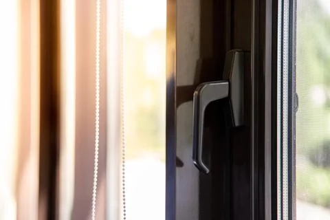Window handle on a brown metal-plastic window through which the sun shines Stock Photos
