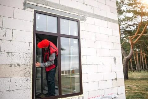 The window installer adjusts the hinges and checks new windows in the cottage Foto stock