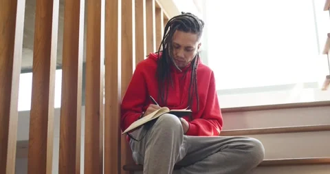 Window light causing man writing in notebook with pen on staircase pausing then Stock Footage 340010074
