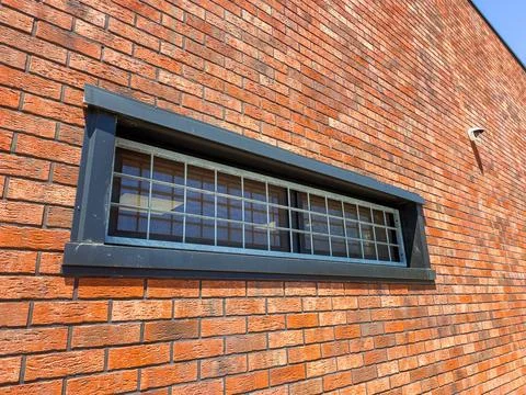 A window with metal bars is placed in a brick wall under clear blue skies. Br Stock Photos