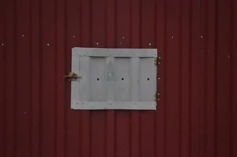 A window with a metal frame is on a red wall. Stock Photos