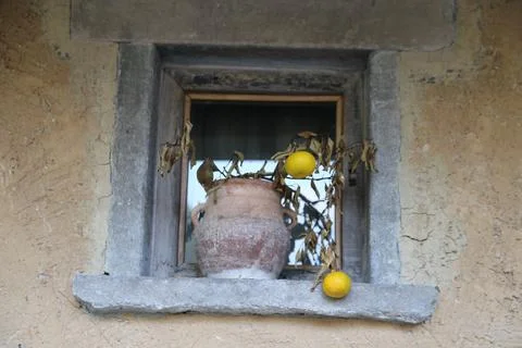 A window with an old clay jar on the windowsill, dried lemons hanging from .. Stock Photos