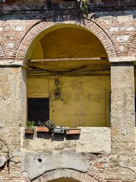Window with plants in a stone wall in a building in an old town under clear s Stock Photos