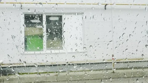 A window with raindrops on it and a person standing in front of a building Vidéo 281133874