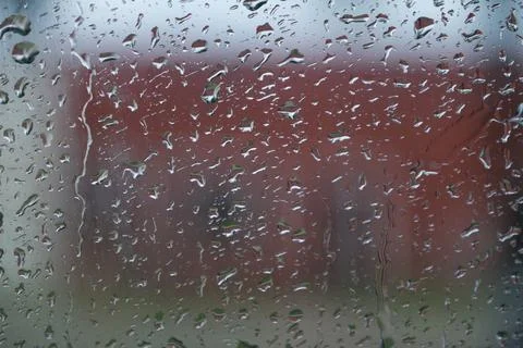 A window with raindrops on it and a red building in the background cold winte Stock Photos