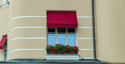 A window with a red awning and a window box with red flowers Stock Photos