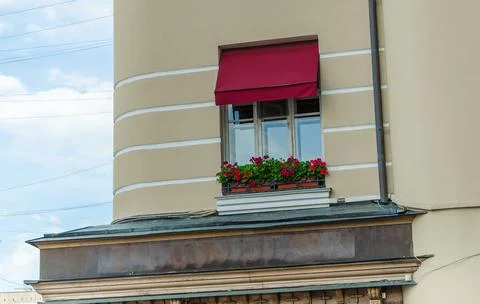 A window with a red awning and a window box with red flowers Stock Photos