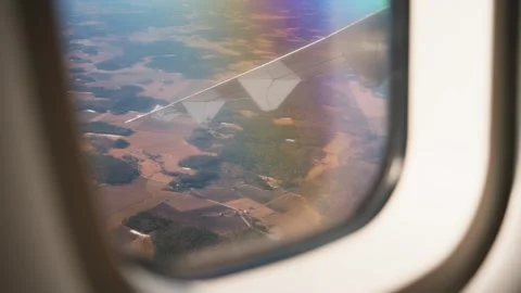 Window-seat view of an airplane wing above patchwork countryside, with rainbow Stock Footage 333655732