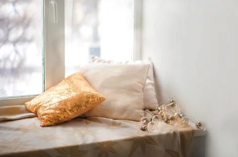 Window sill and pillows, empty space. Gold pillow with sequins, window, garland. Stock Photos