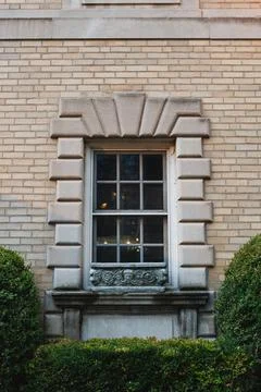 A window with a stone frame sits on a brick wall. Green bushes are on either  Foto stock
