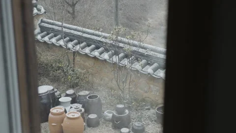 Window View of Korean Ceramic Pots Laid out by a Stone Wall as it Snows while Stock Footage 340860031