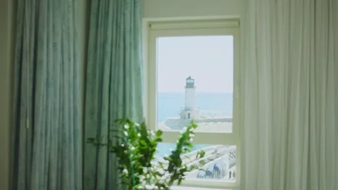 Window view of white lighthouse on curved breakwater by blue sea Stock Footage 327013711