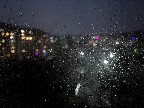 The window is wet from rain. Theme Background.Night city behind wet glass. Urban Stock Photos