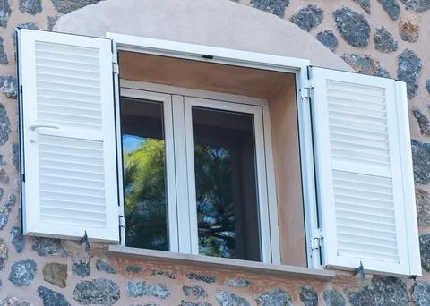 Window with white plastic shutters in a stone wall. Stock Photos