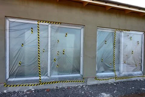Windows of a house under construction covered with protective plastic film. Stock Photos