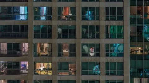 Windows of the multi-storey building with lighting inside and moving people i Stock Photos