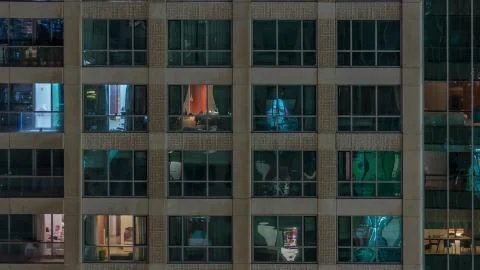 Windows of the multi-storey building with lighting inside and moving people i Stock Photos