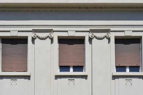 Windows with pulled down roller shutters on white classic facade Stock Photos