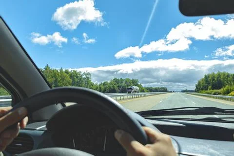 Windscreen view of nature road sky hand of man on the steering wheel in a spr Stock Photos