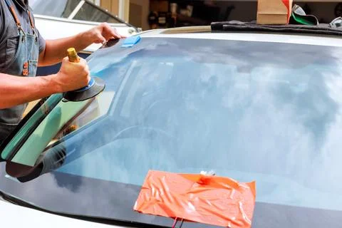 Windshield replacement technician works on fixing damaged car window in repair Stock Photos