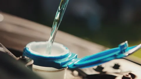 Windshield washer fluid is poured into the windshield wiper reservoir of a car Stockbeeldmateriaal 254057539