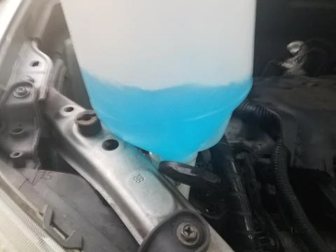 Windshield wiper fluid bottle and under a car's hood Stock Photos