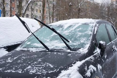 Windshield wipers of parked car rest on snow-covered glass Stock Photos