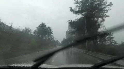 Windshield wipers sweeping raindrops during rainy drive near suburban Vidéo 306793888