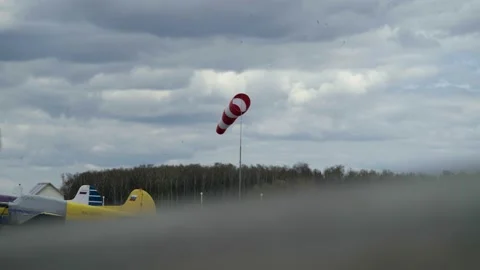 Windsock develops in the wind against the background of a cloudy sky and forest Vidéo 153603814