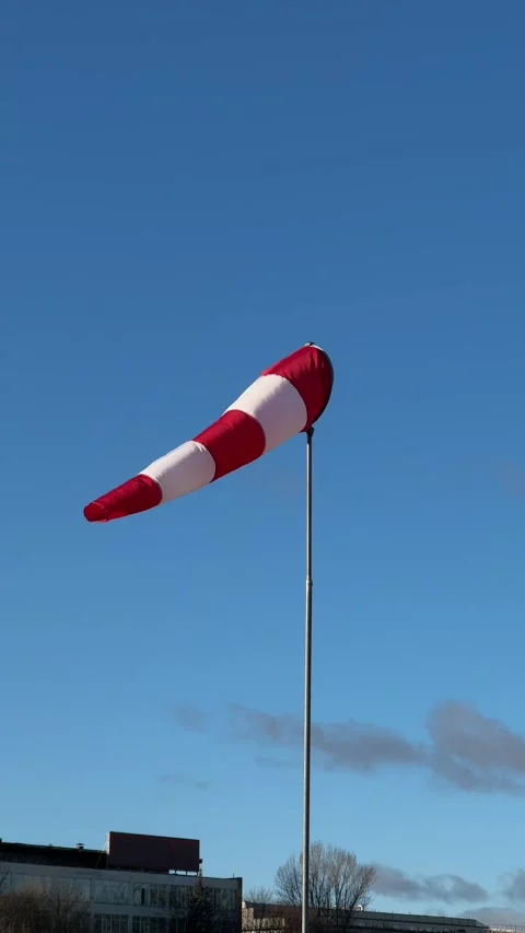 Windsock mounted on a pole against a clear blue sky with industrial buildings Stock Footage 294036952