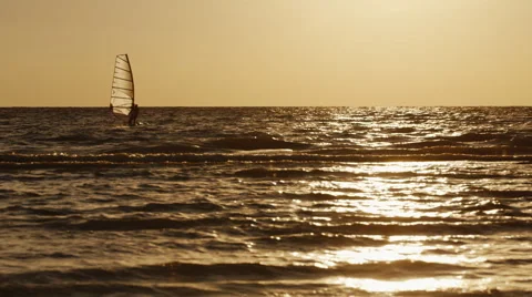 Windsurfer floats on a board with a sail at sunset Stock Footage