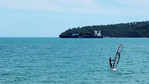 Windsurfer sailing across the sea with a cargo ship Stock Footage 337254863