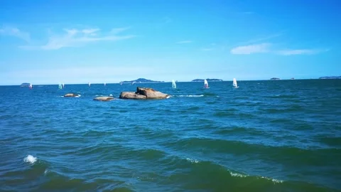 Windsurfers gliding across blue ocean waters near coastal rock formations Stock Footage 341999038