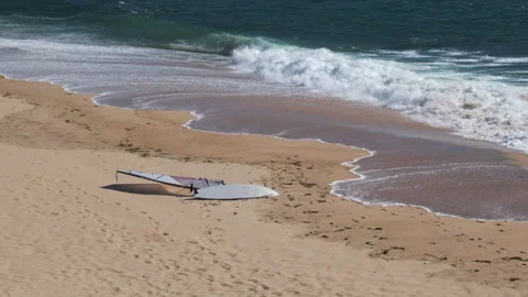 Windsurfing board lying on sandy beach as waves break on shore slow motion Stock Footage 132210144
