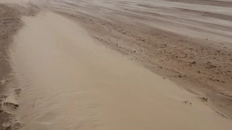 Windswept dry sand particles quickly snaking along a deserted beach Stock Footage 145901568