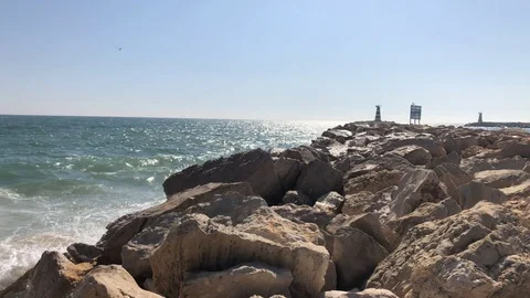 Windy view of waves crashing on rocks, with lighthouse in distance Stock Footage 98413907