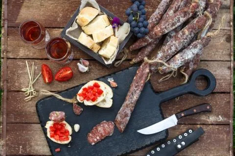 Wine and appetizers set. Bread, dry cured pork meat sausage, tomato on rustic Stock Photos